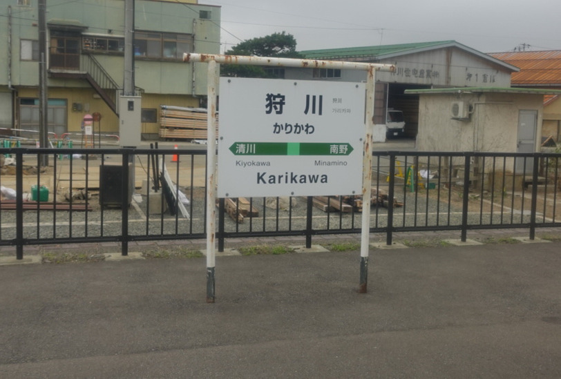 列車の車内から狩川駅の駅名標が見える